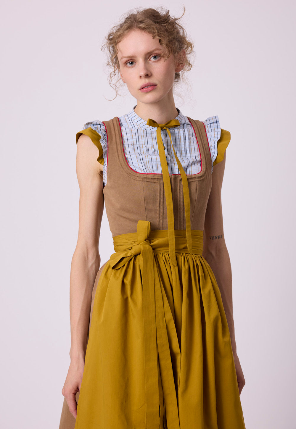 Model wearing the Vroni Blouse Karo with checked cotton fabric, pintucks, ruffled cap sleeves and detachable bow tie.